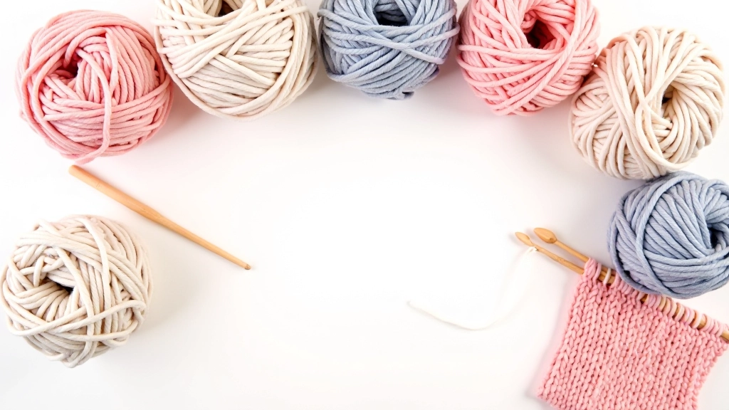 Colorful yarn balls and crochet hooks arranged on white surface with finished crochet project in background